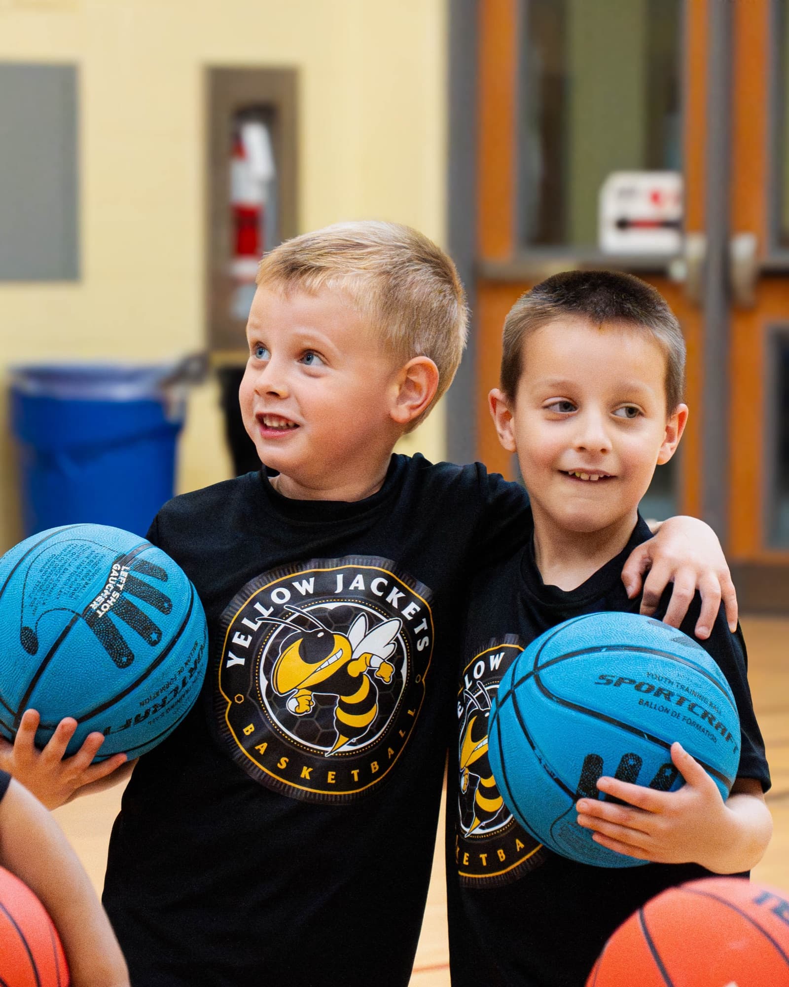 Two young players with arms around each other, holding basketballs